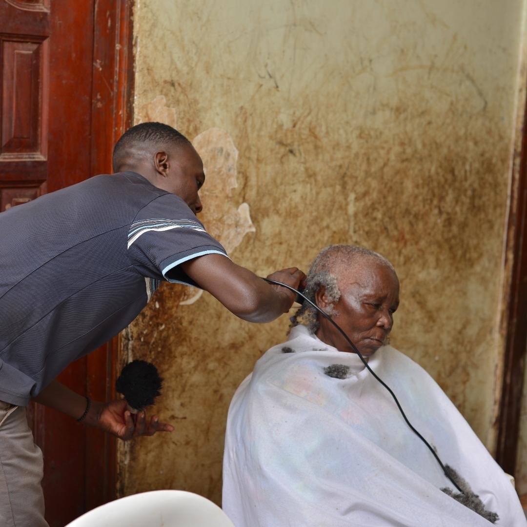 Young man trimming an elderly woman's head hair.